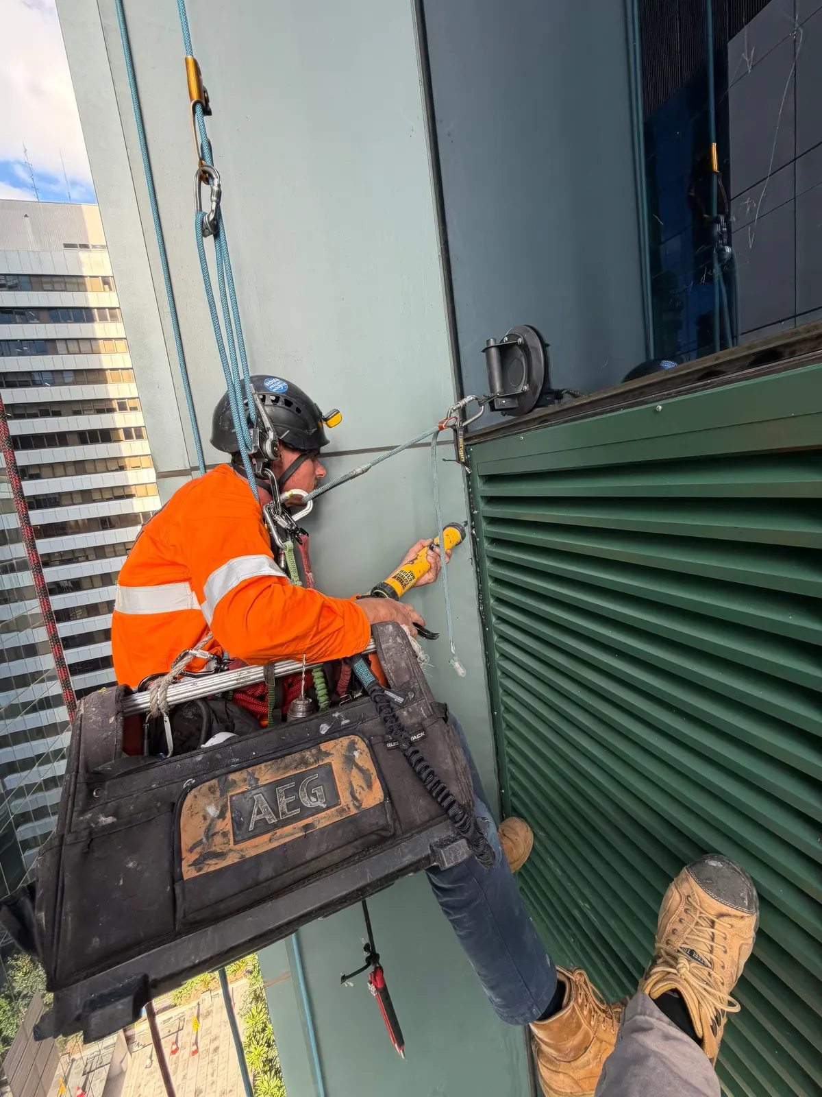 Konstruct rope access technician on ropes sealing a newly installed green fresh air louvre into a Brisbane CBD curtain wall facade