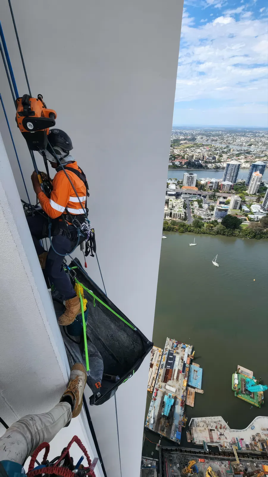 Konstruct rope access technician abseiling high on a white tower façade above the Brisbane River, the city and river far below
