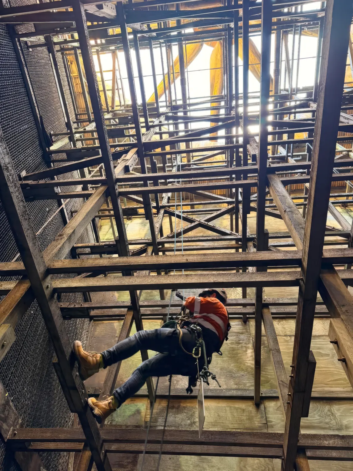 Rope access technician descending inside the timber-and-steel internal frame of an ageing cooling structure