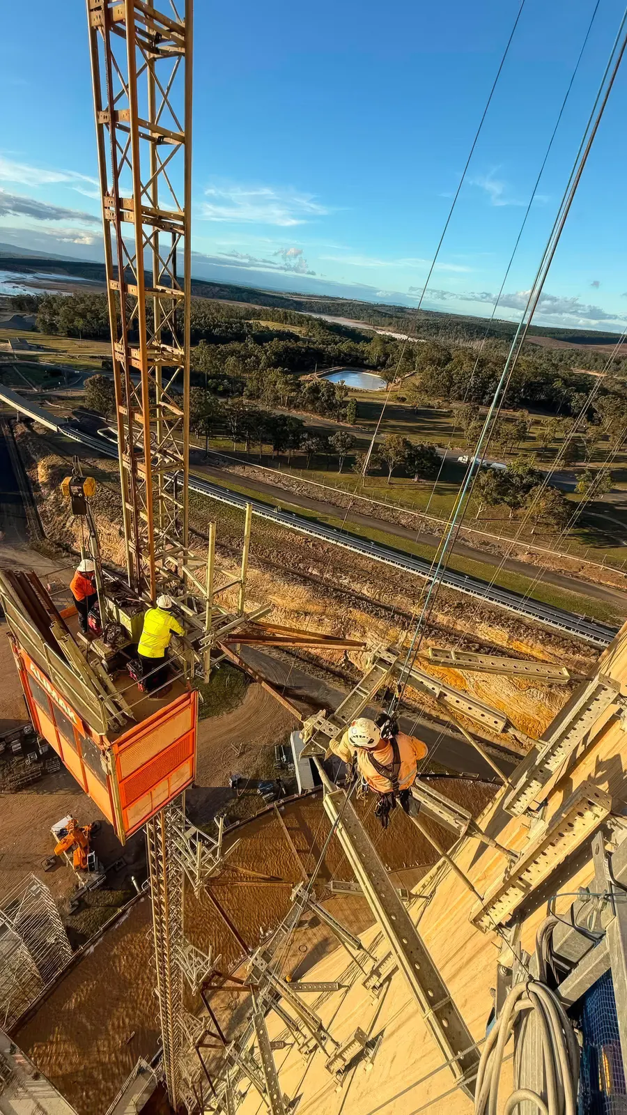 Konstruct crew installing ring scaffold and access at the crest of a Queensland power-station cooling tower, rural landscape far below