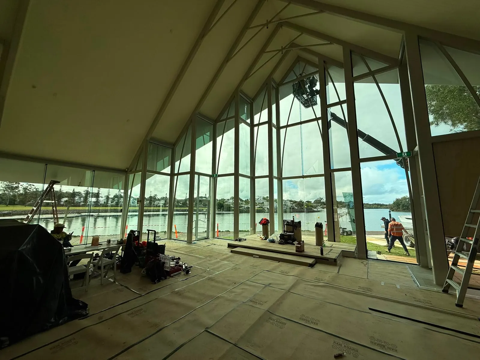 Interior of the fully glazed Sanctuary Cove chapel during facade remediation, its vaulted roof and steel mullions framing the waterfront beyond